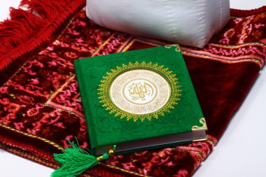 Yeşil El-Kuran, Müslüman kutsal kitabı, üzerinde Arapça harfler olan kırmızı dua eden bir halı.