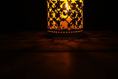 Karanlık gecede bir ışık kaynağı olarak parlayan kırsal ahşap bir masanın üzerindeki mum fenerleri.