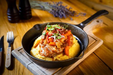 cooked pork with polenta and vegetables with microgreens served in a rustic cast iron pan clipart