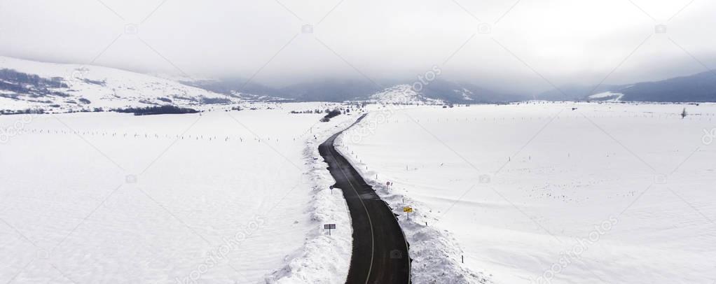 Long road stretches through the snowy landscape, aerial view