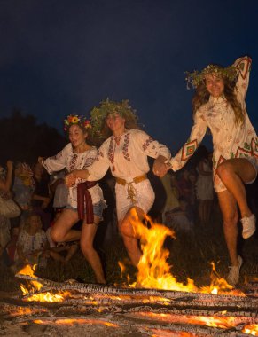 Pirogiv, Kievskaya oblast / Ukrayna - 07.06.2013. Ukrayna gömlekli kızlar ateşin üzerinden atlıyorlar. Ivan Kupala tatili.