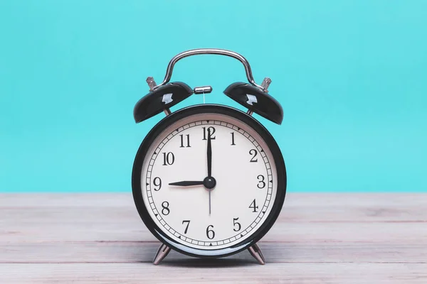 Un reloj despertador negro retro en tablero de madera con fondo verde — Foto de Stock