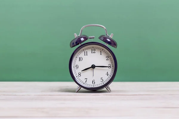 緑の背景を持つ木製ボード上のブラックレトロ目覚まし時計 — ストック写真