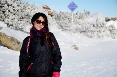 Kış örtüsü içinde gülümseyen güzel bir kadın ve karlı arka planda gözlük.