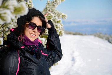 Kış örtüsü içinde gülümseyen genç bir kadın ve karlı arka planda gözlük.