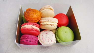 Mutfak masasının arkasında renkli badem kurabiyeleri olan kutu.