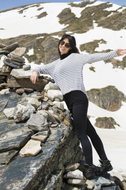 Güneş gözlüklü güzel bir kadın. Arka planda dağlarda kayalar var.