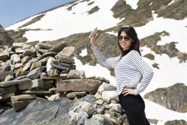 Güneş gözlüklü güzel bir kadın. Arka planda dağlarda kayalar var.