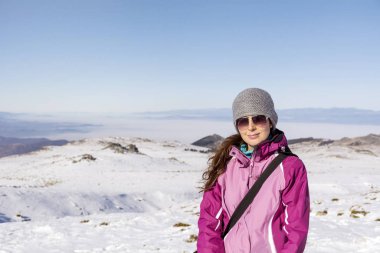 Kış örtüsü içinde güzel genç bir kadın ve karlı arka planda gözlük.