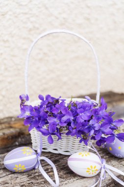 Beyaz arka planda mor çiçekli beyaz sepet ve Paskalya yumurtaları