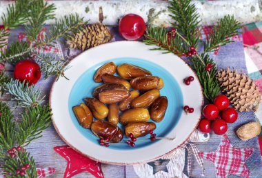 Tahta masadaki seramik tabakta kurumuş tarihler elma, tümsek ve ladin dallarıyla.