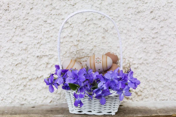 Witte Mand Met Paarse Bloemen Paaseieren Witte Muurachtergrond — Stockfoto