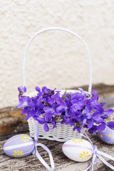 Witte Mand Met Paarse Bloemen Paaseieren Witte Muurachtergrond — Stockfoto