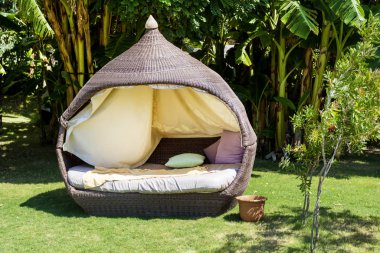 Yeşil egzotik bir bahçede muz ağaçlarıyla yastıklı Rattan Sunbed 'i rahatlatıyor. 