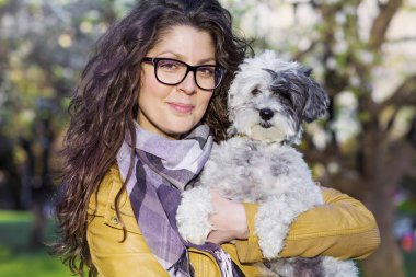 Güzel, gülümseyen kadın parkta sevimli köpeğini kucaklıyor. Evcil hayvan ve doğa sahibi.