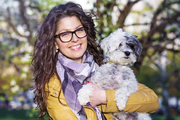 Güzel, gülümseyen kadın parkta sevimli köpeğini kucaklıyor. Evcil hayvan ve doğa sahibi.