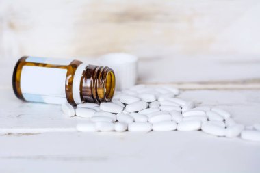 Cam şişedeki haplar beyaz tahta arka planda.