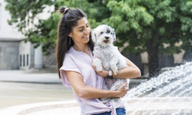 Güzel, gülümseyen bir kadın sokakta sevimli havan köpeğine sarılıyor. Şehirde evcil hayvan ve sahibi.