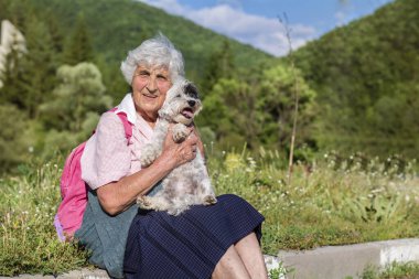 Mutlu kıdemli kadın doğada havan köpeğini kucaklıyor.