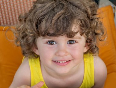 Kıvırcık saçlı küçük mutlu kızın portresi. Yukarıdan gülümseyen bir çocuğun yakın çekimi.