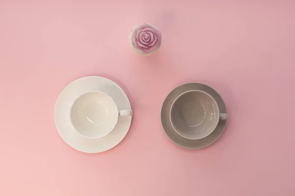 ピンクの背景に2つの空のカップとバラのキャンドル. — ストック写真
