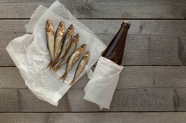 Tahta arka planda bira şişesiyle tütsülenmiş ringa balığı.