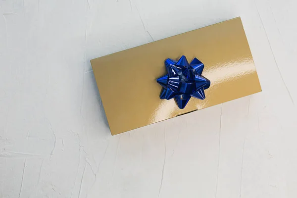 Golden box with a gift and a blue bow on a light texture backgro