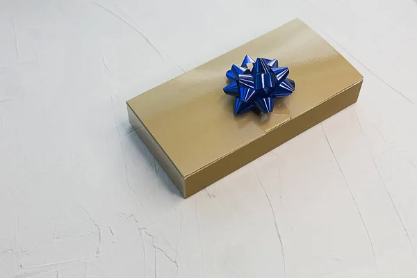 Golden box with a gift and a blue bow on a light texture backgro
