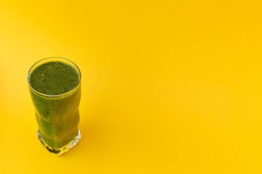 Parlak sarı arka planda yeşil bitkilerle dolu bir bardak. Model ve projeniz için minimalist konsept. 