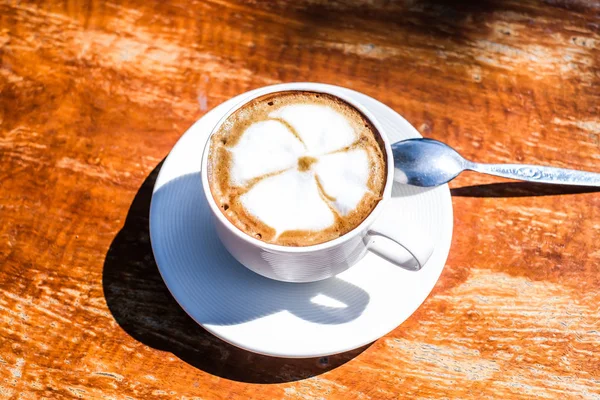 Bir bardak kapuçino ve ahşap masa üzerinde güzel bir latte sanatı. Birbirine aşık çiftler için sabah kahvesi, sıcak kahve, üst manzara..