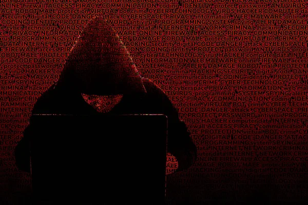 The silhouette of a hooded hacker working at a laptop, against a