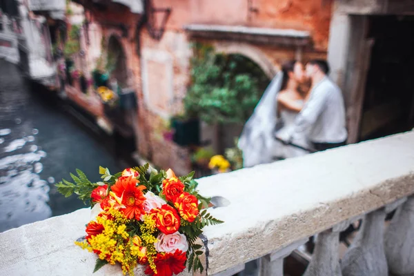 在前台的婚礼花束，在背景的新娘和新郎在威尼斯 — 图库照片