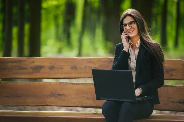 Business lady sitting on a bench with a laptop and talking on the phone
