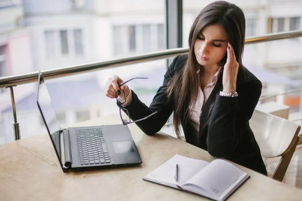 Una mujer de negocios está sentada en la oficina durante mucho tiempo y tiene un dolor en la cabeza. — Foto de Stock