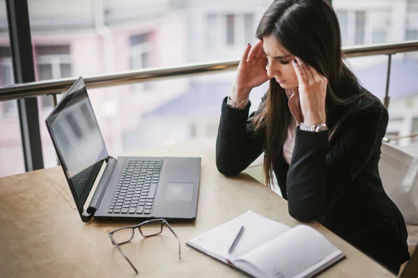 A business lady is sitting in the office for a long time and she has a pain in her head