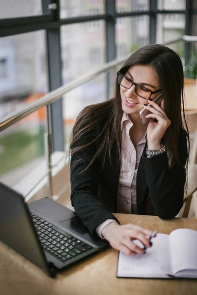 Mujer de negocios sentada en una oficina blanca y recibiendo llamadas en la mesa — Foto de Stock