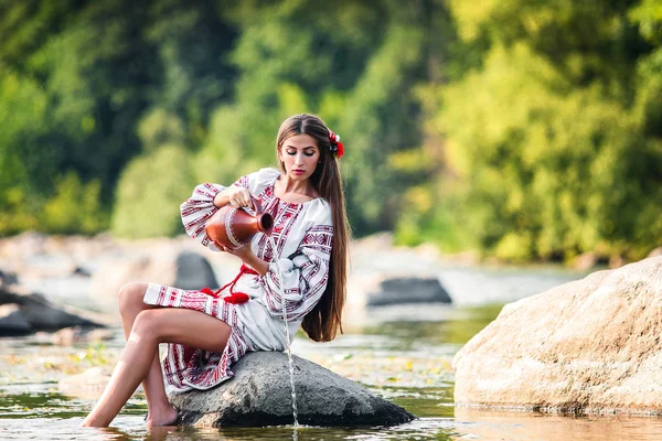 Flicka Broderad Klänning Sitter Sten Med Kanna Nära Vattnet — Stockfoto