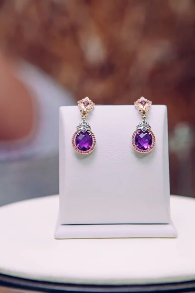 set of earrings with gold plating and with purple jade in the form of a circle stands on a box