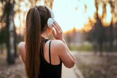 bluetooth kulaklıklar müzik günbatımında parkta dinlemek spor kıyafetli neşeli kız