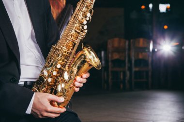 bir müzisyen bir takım elbise ve beyaz bir gömlek oturan ve saksafon elinde Sahne Alanı'nda oynuyor.