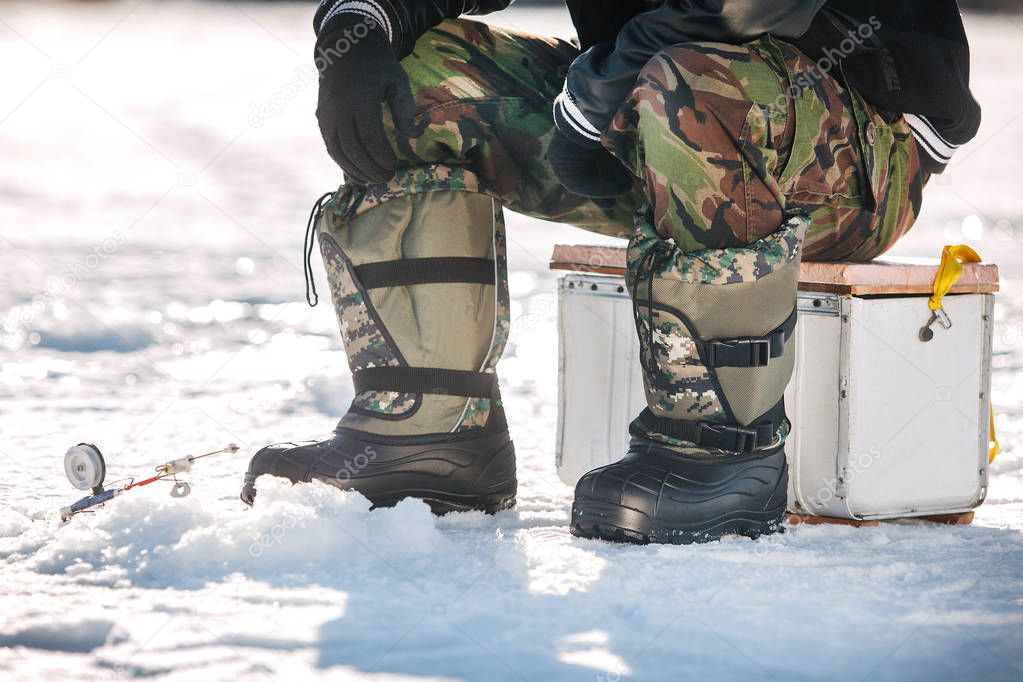 fisherman sits and catches fish on a chair on the ice in felt boots in the winter