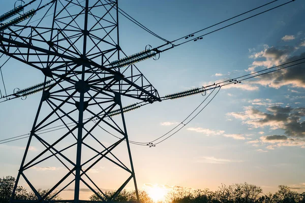 pillar of high-voltage power lines is standing in the field on the background of the blue sky