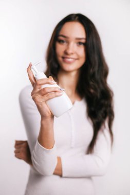 Kız elinde beyaz arka planda bir şişe tutuyor.