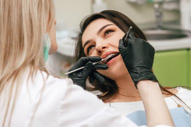 Dişçi yeşil ofisteki bir müşterinin dişlerini inceliyor.