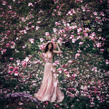 spring girl stands in a beautiful garden and a lot of magnolia flowers