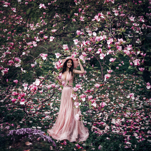 Spring girl stands in a beautiful garden and a lot of magnolia flowers