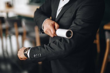 Bir adam siyah ceketi silindirle temizler.