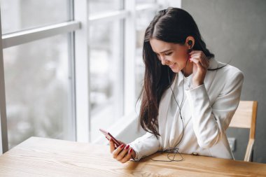 Kadın masada kulaklıkla müzik dinliyor.