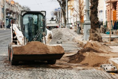 Şehirde küçük bir traktör çalışıyor, kovada kum getiriyor.