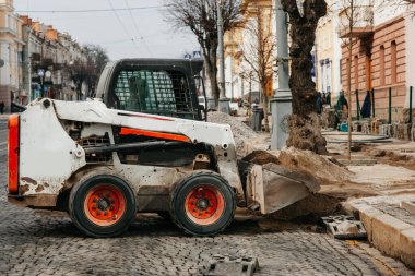 Şehirde küçük beyaz traktör çalışıyor, şehirde yol onarımı yapıyor.